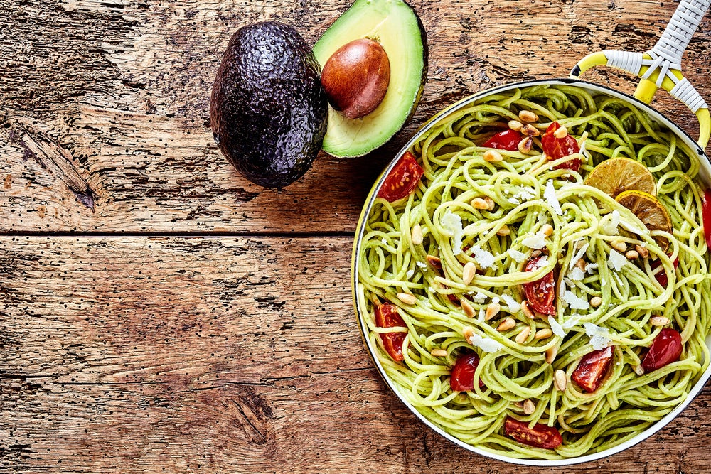 Image of a bowl of pasta with tomatoes in it and avocado on the side.