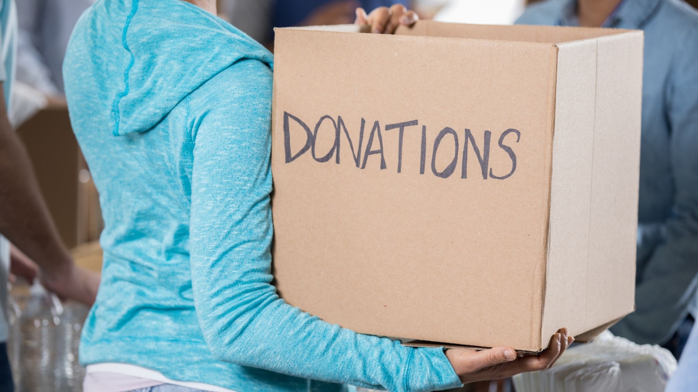 A woman holds a cardboard box that says "Donations." She wants to donate used tri gear.