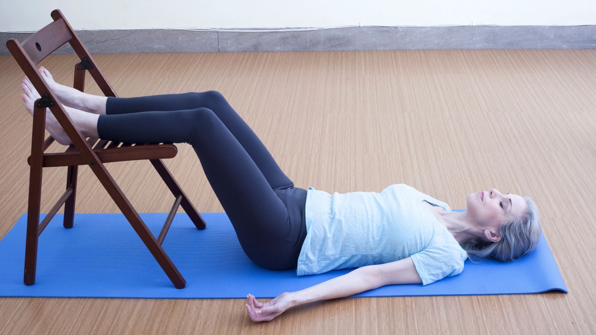 A woman lies on her back with her legs elevated on a chair.