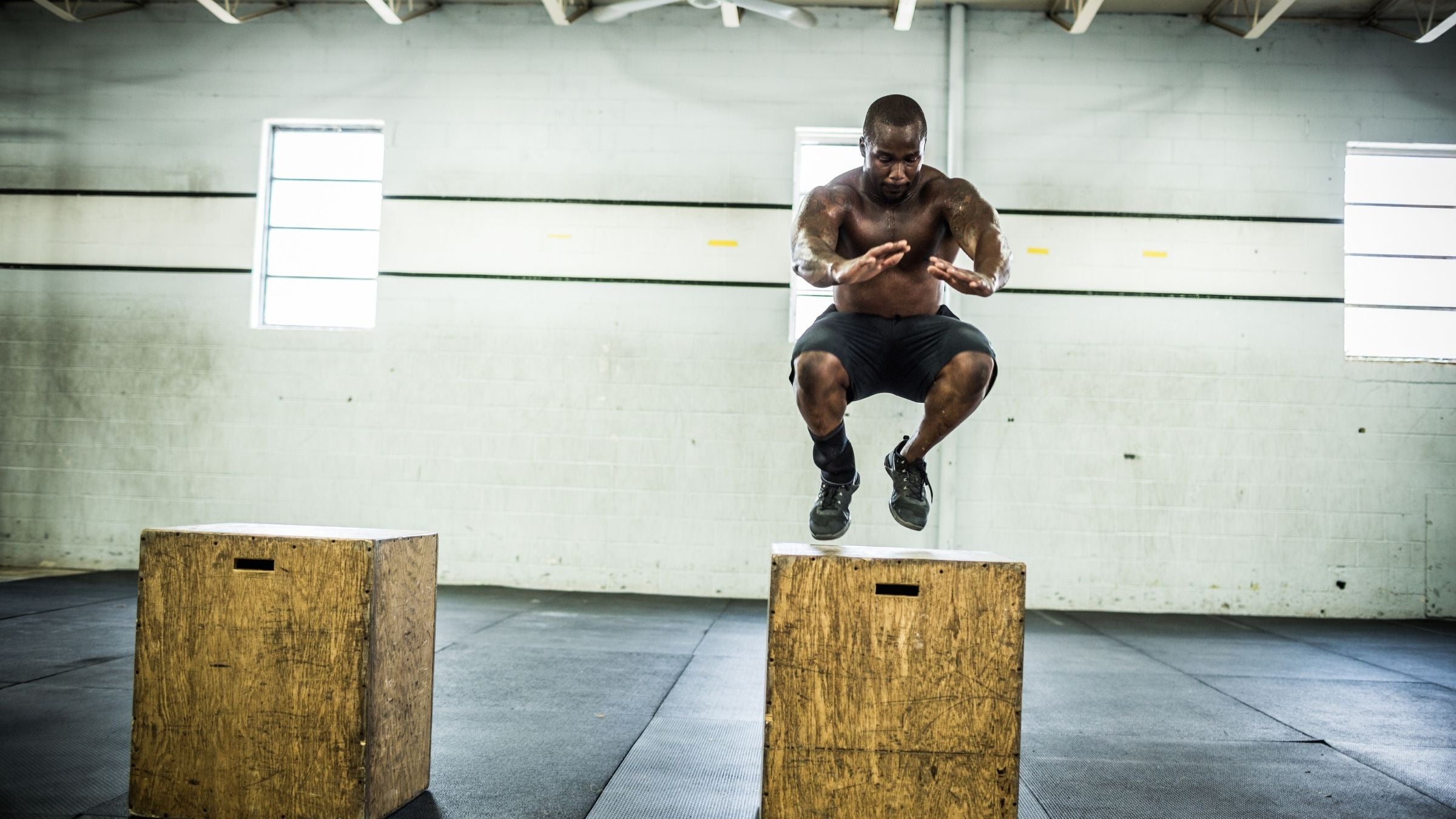 A man in athletic shorts and shoes jumps onto a wooden box.