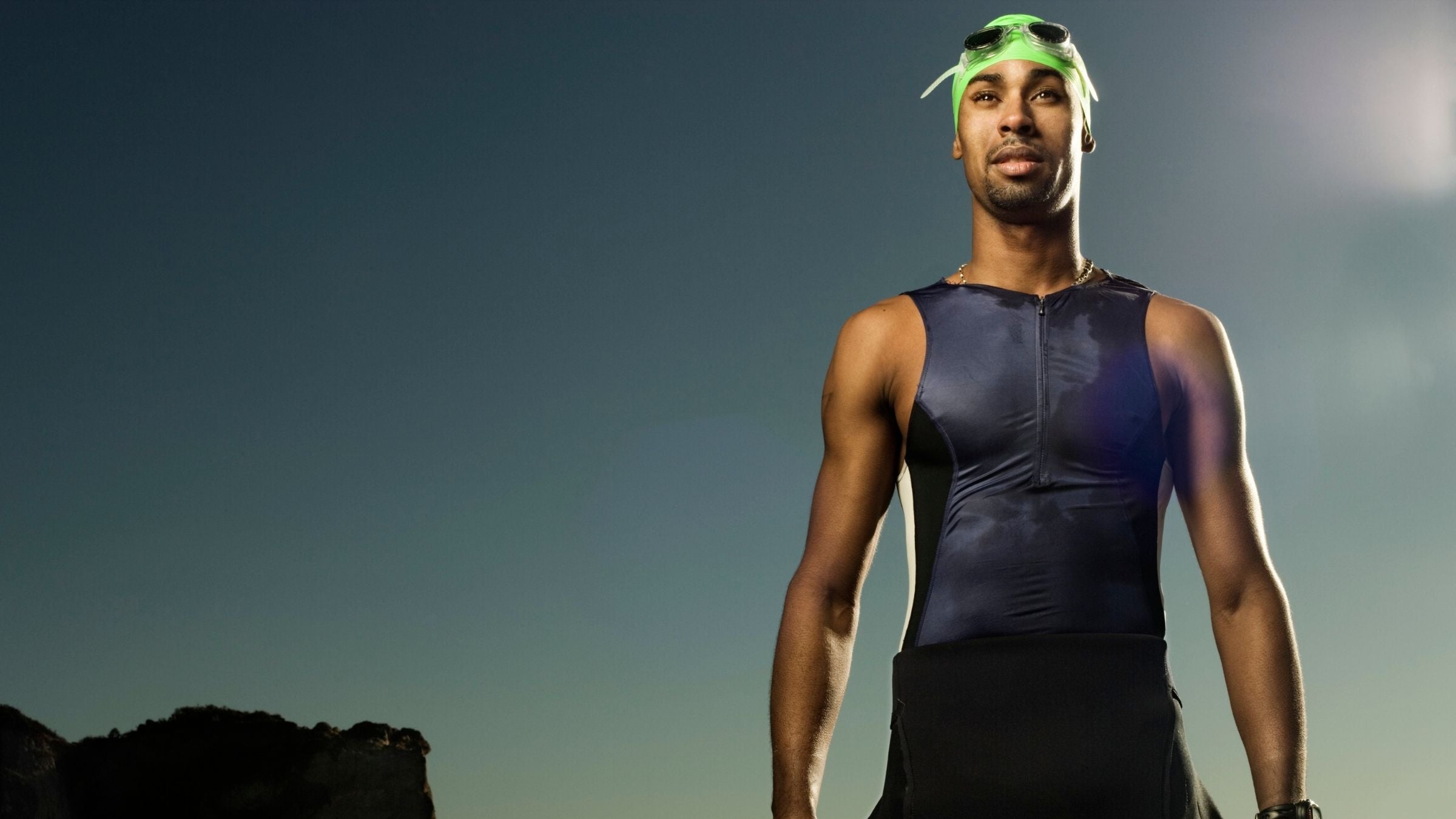 A man stands in a triathlon suit, swim cap, and swim goggles, ready to start a race.