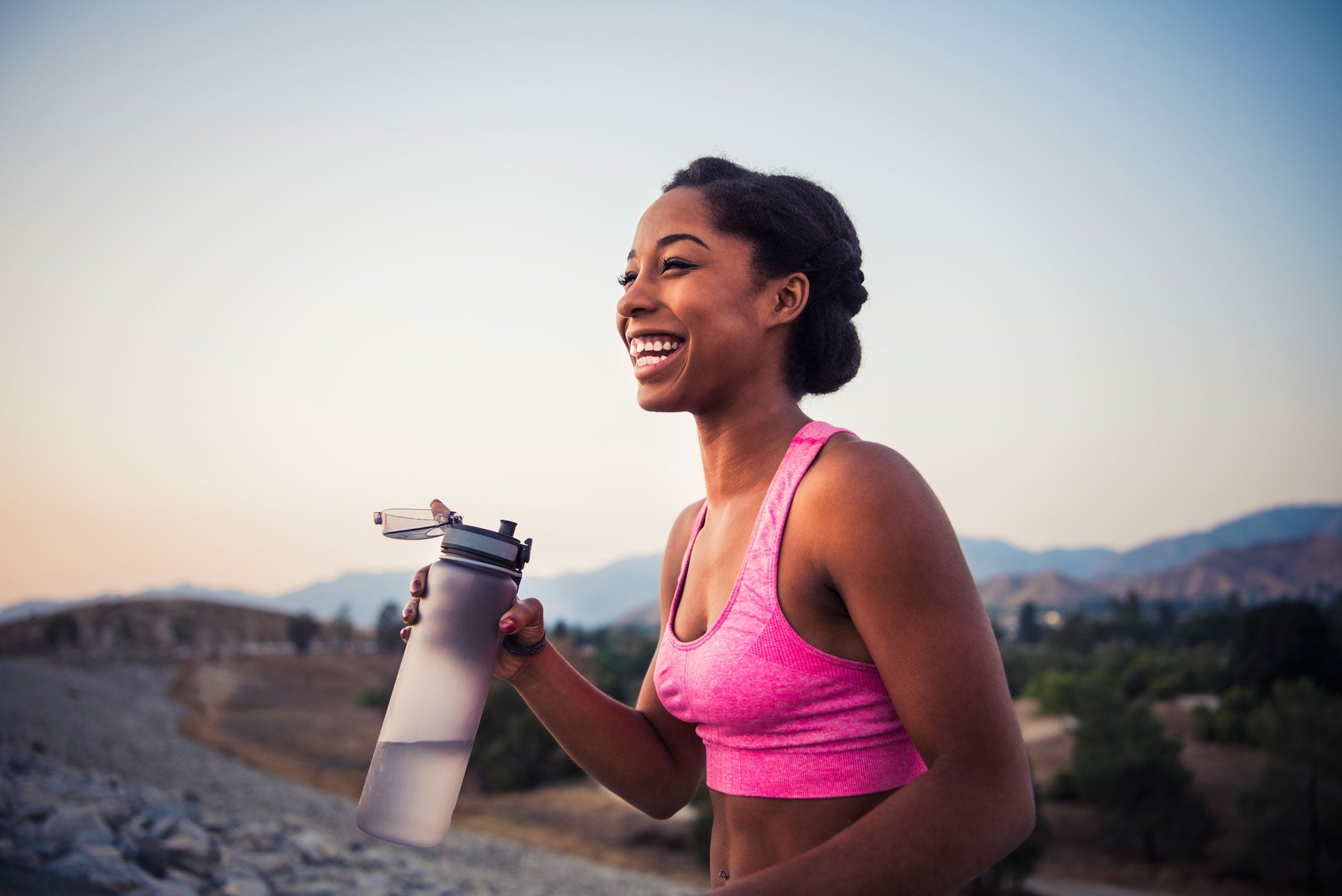 Smiling woman with water bottle on a hill at sunset