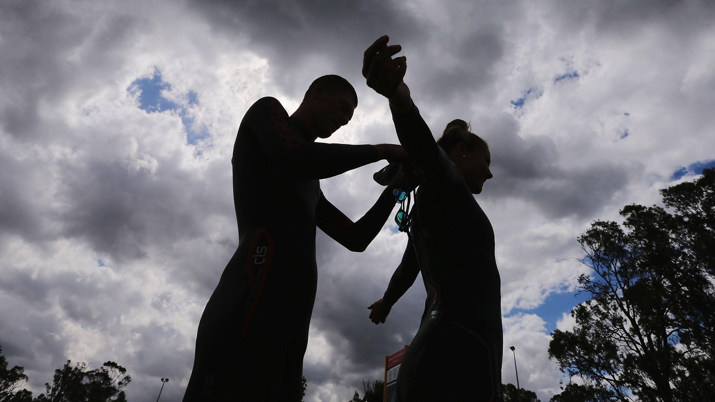 A triathlete helps another athlete put on a triathlon wetsuit.