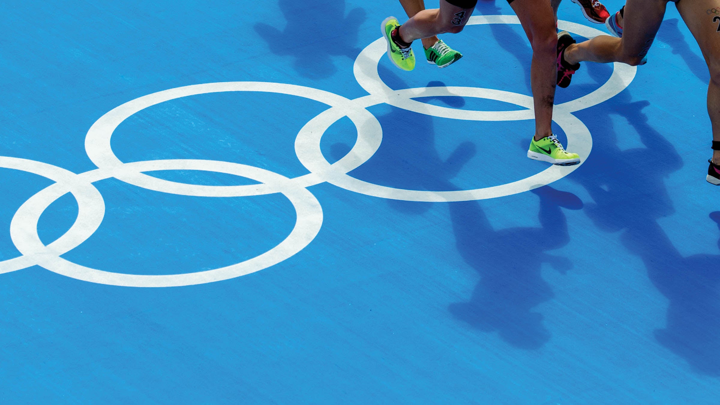 Athletes run past the Olympic rings painted on the ground