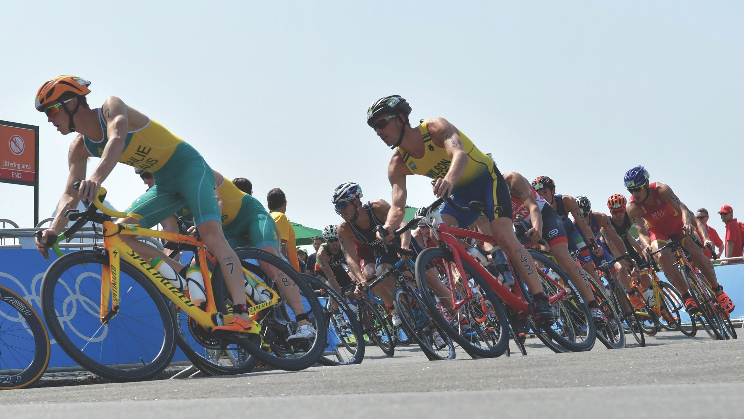 A large group of male triathletes round the corner of the bike course at a draft-legal triathlon.
