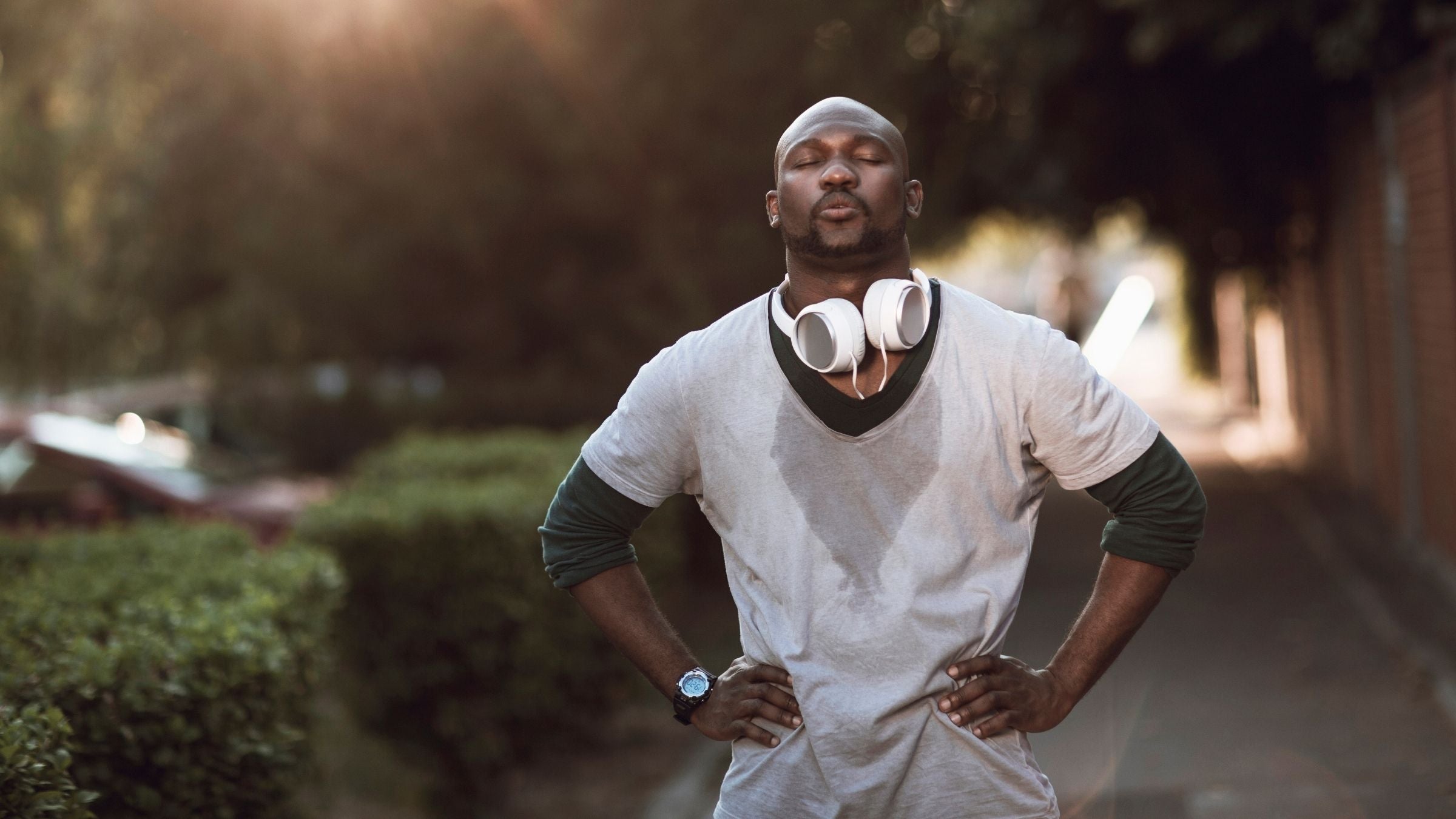 A man, covered in sweat, looks fatigued as he takes a break during a run.