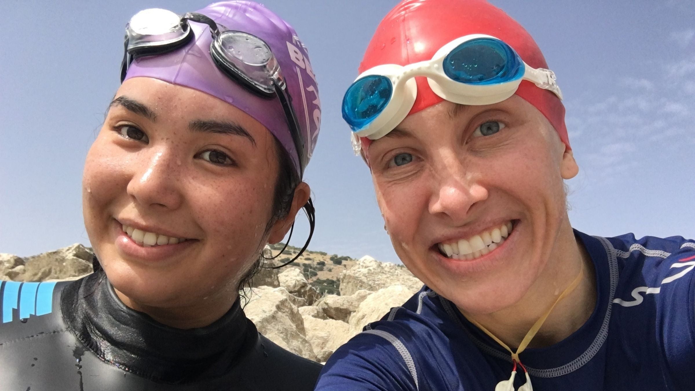 Two women in wetsuits and swim caps take a selfie after a swim.