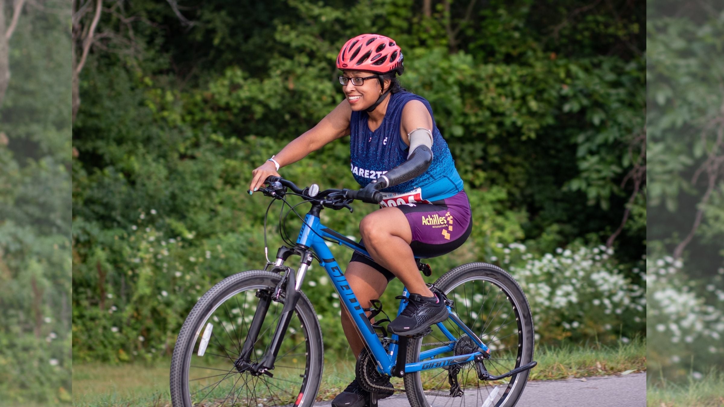 A woman rides a bike in a triathlon. She has an arm limb difference and is wearing a prosthetic hand.