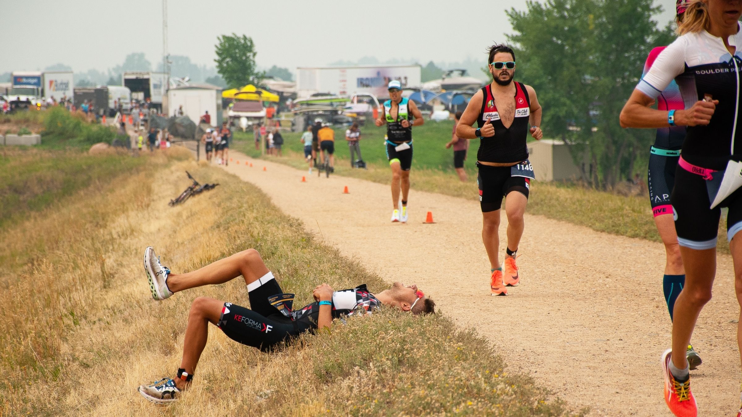 A triathlete is laying on the ground experiencing bad pain while racing. Other triathletes are running past.