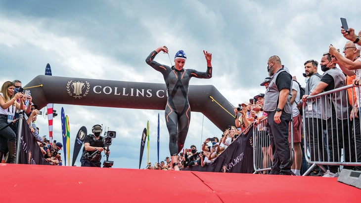 Woman in a full body wetsuit running past a checkpoint with a film crew behind her