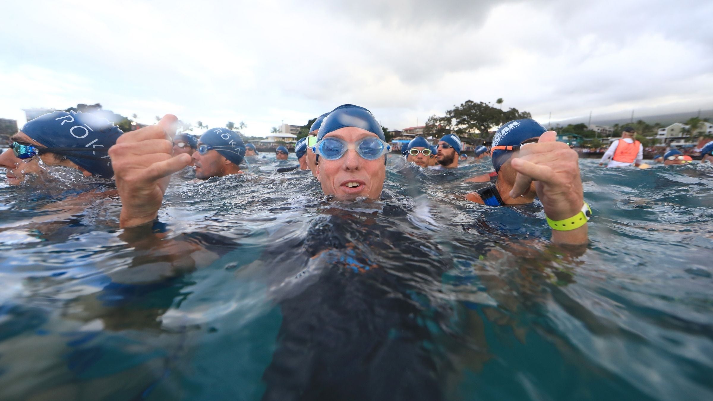 An athlete cracked the code of how to qualify for Kona, and awaits his start at the Ironman World Championship. He is wearing a wetsuit, goggles, and a swim cap while treading water.