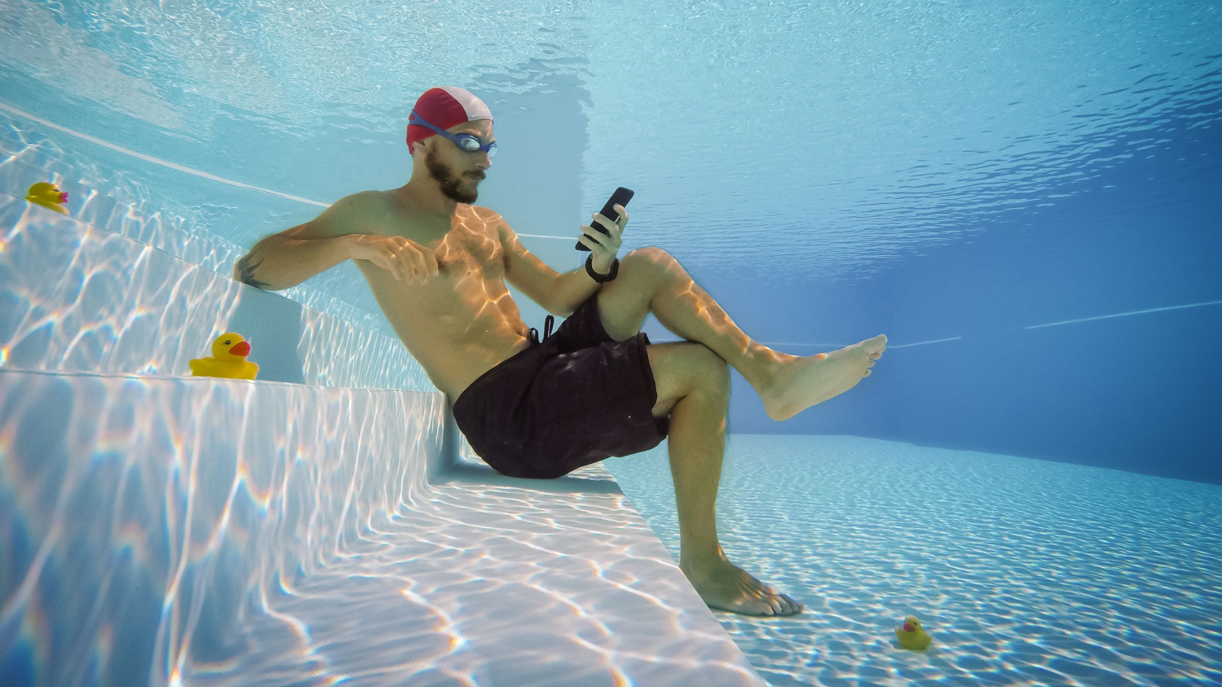 A man scrolls through his phone while underwater, sabotaging swim workout.
