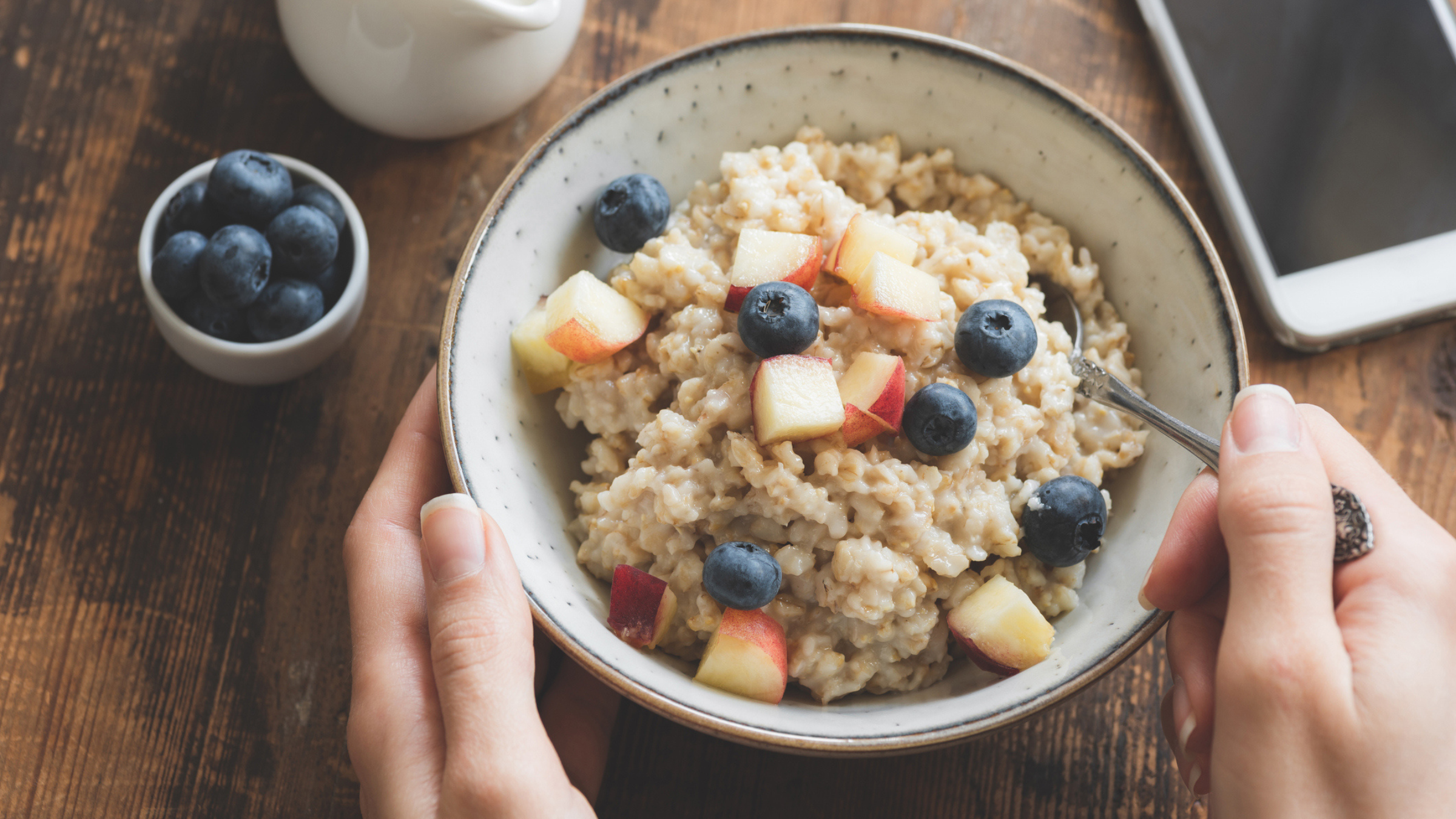bowl of oatmeal with fruit on top set on table with hands around it for recovery carbs after a workout