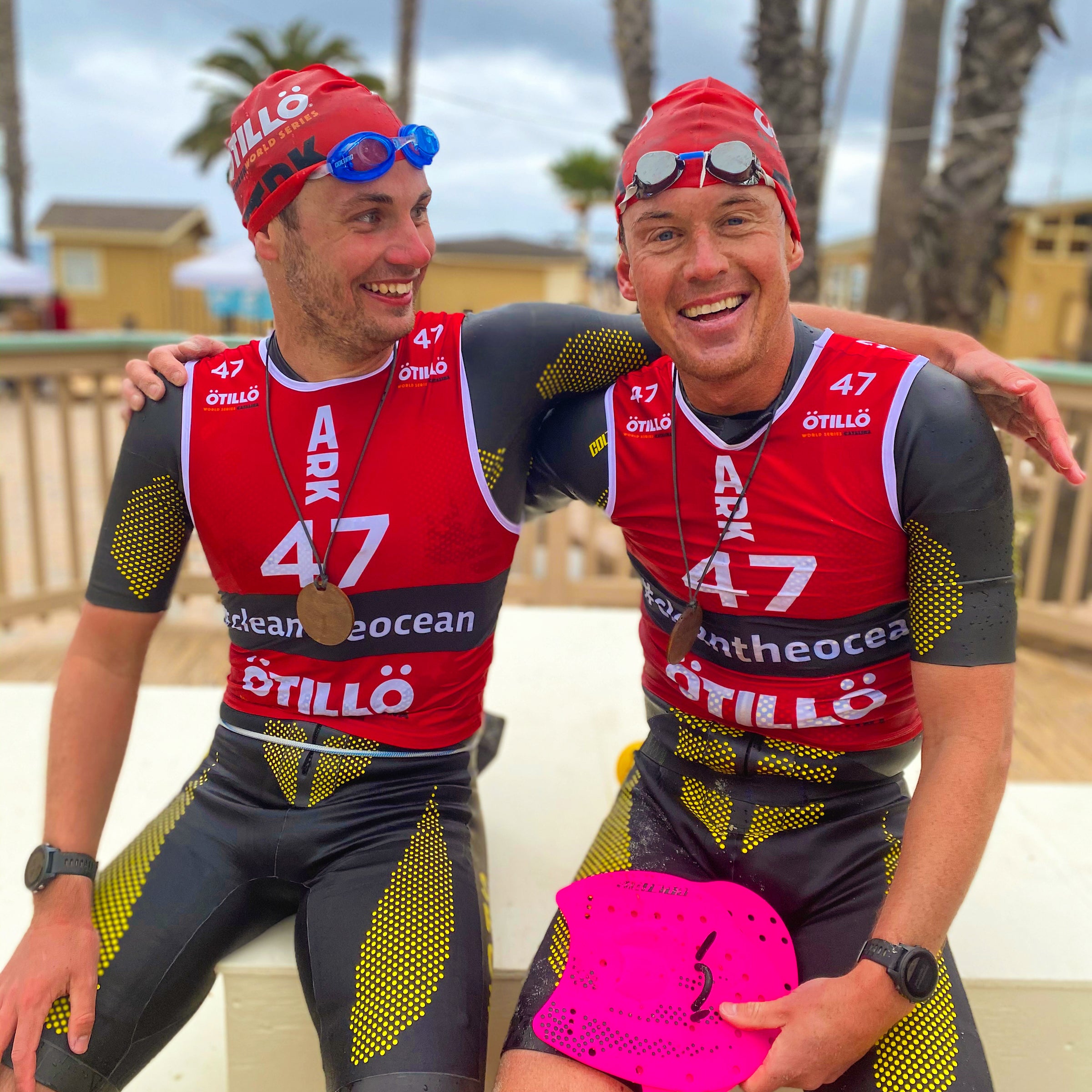 Two men rest in their swimrun gear with arms around each other, smiling