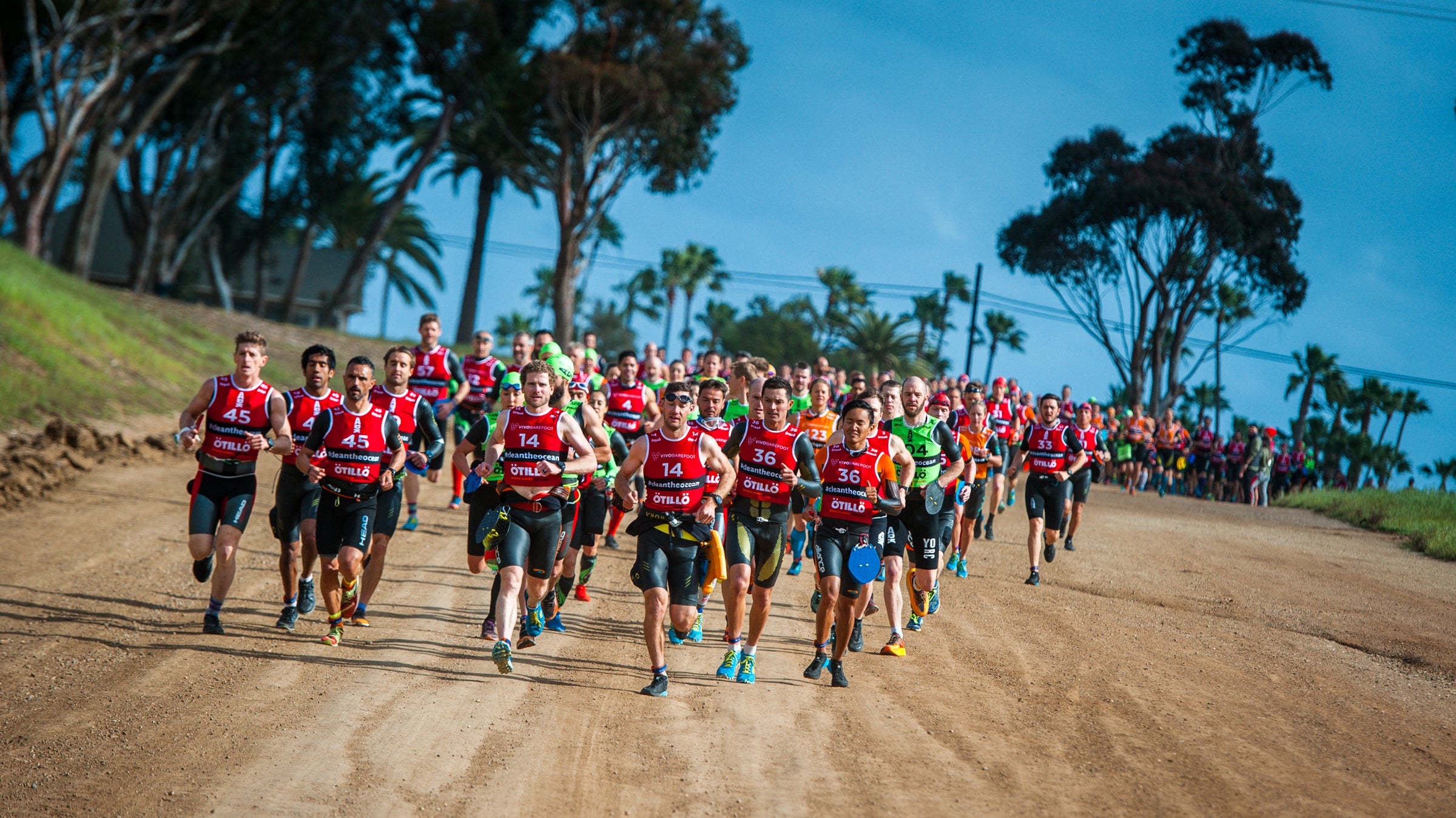 Crowd of swimrunners running toward camera on a tree-lined dirt road